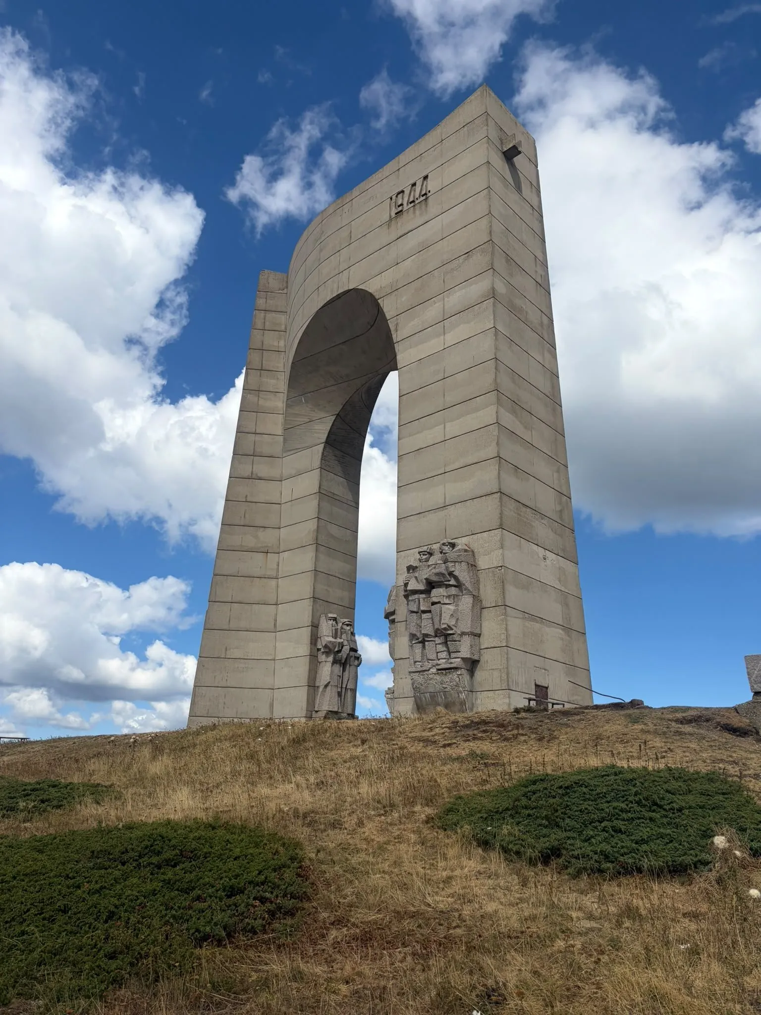 The Arch of Freedom monument on a mountain top under a blue sky with white clouds