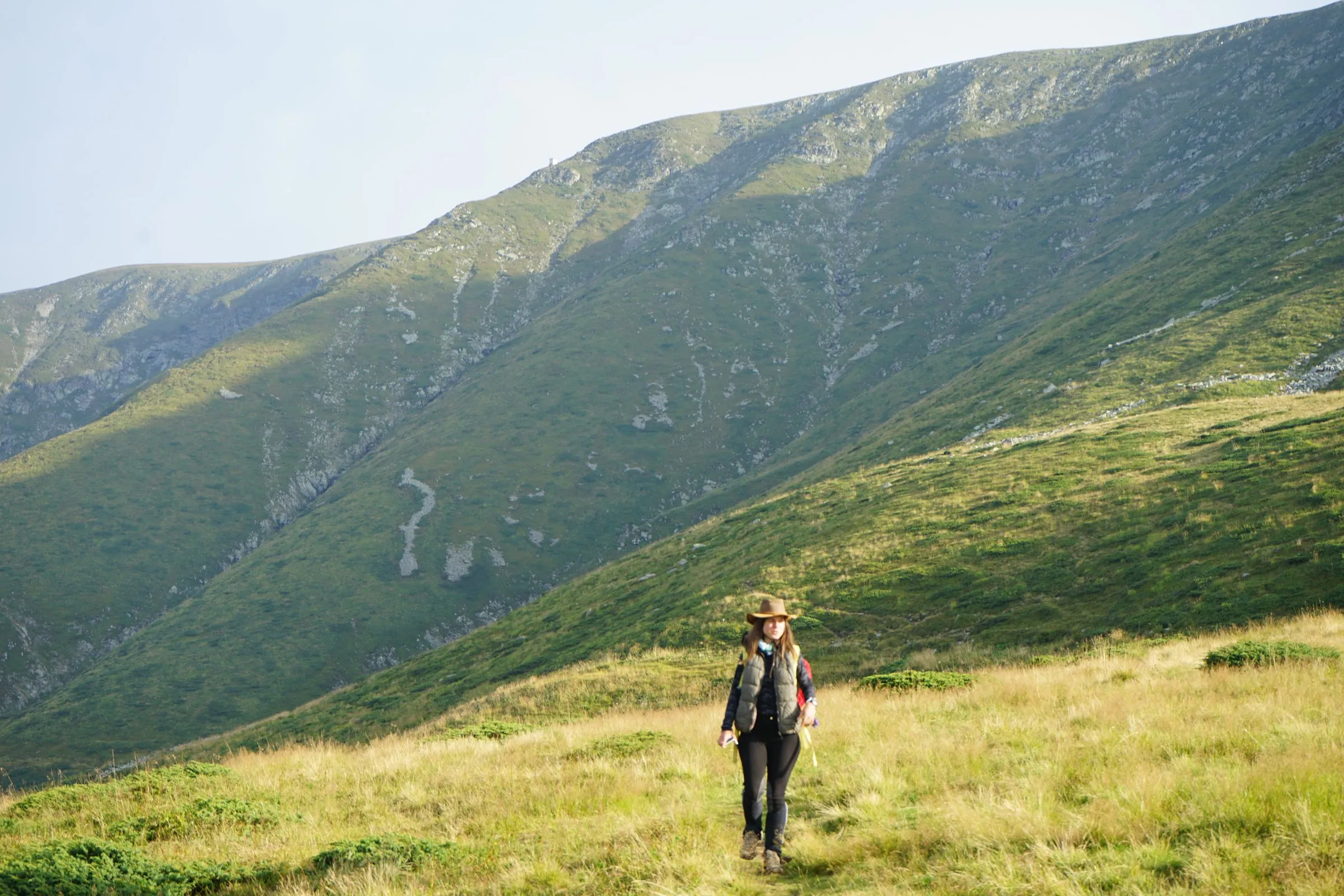 A person in a cowboy hat walking across a wide mountain meadow