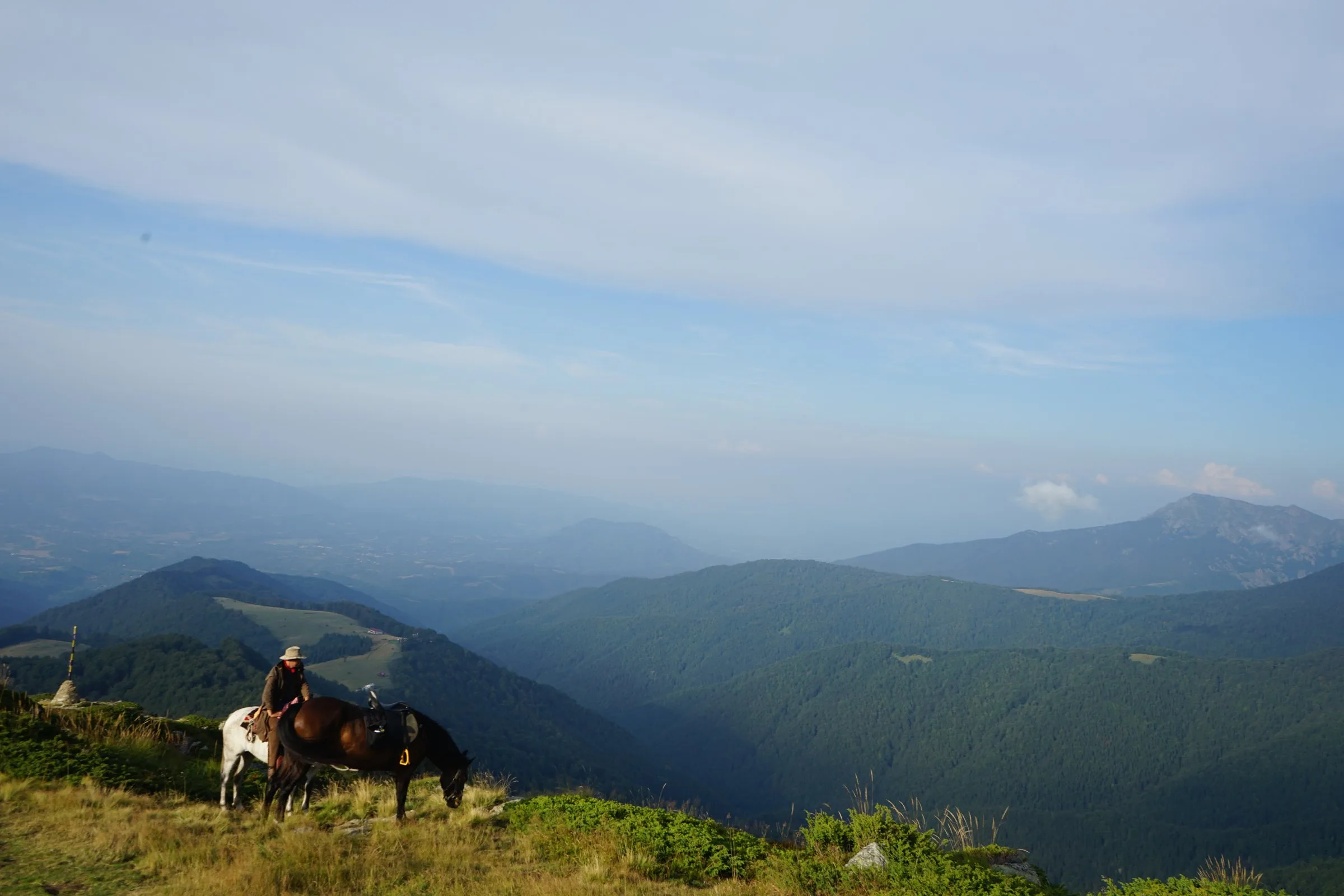 Rider with two horses resting at a lookout above misty Balkan valleys