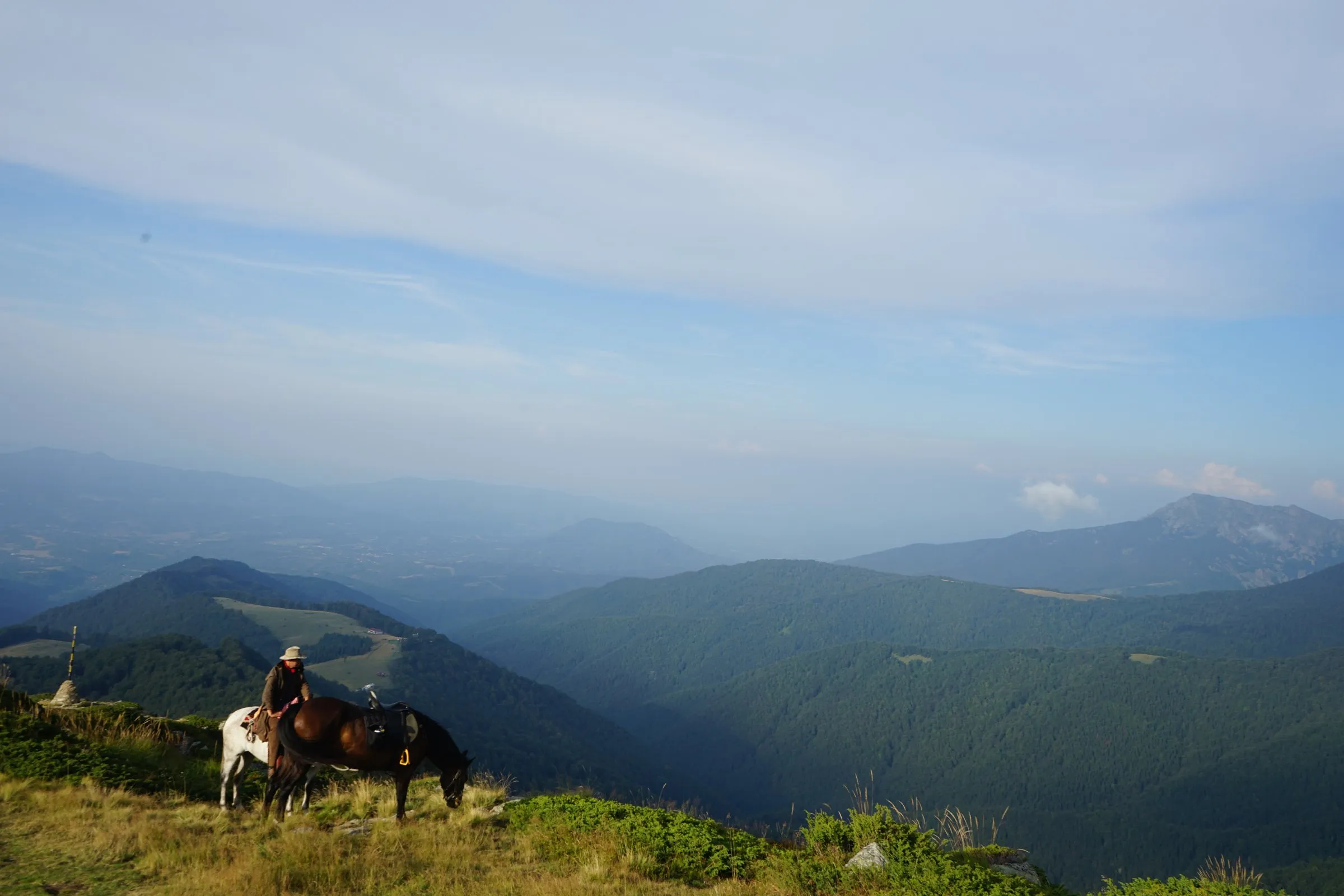 Rider with two horses resting at a lookout above misty Balkan valleys